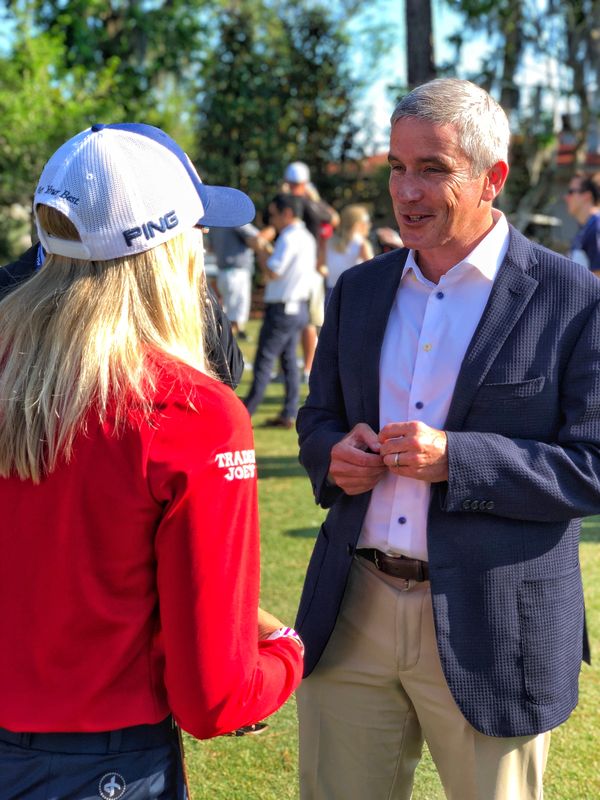Pernilla Lindberg, seen from behind in a red top, talking with Jay Monahan on a lawn