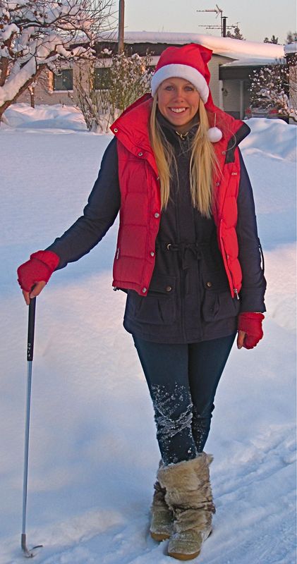 Pernilla Lindberg in a Santa hat and red vest standing in deep snow, holding a golf club